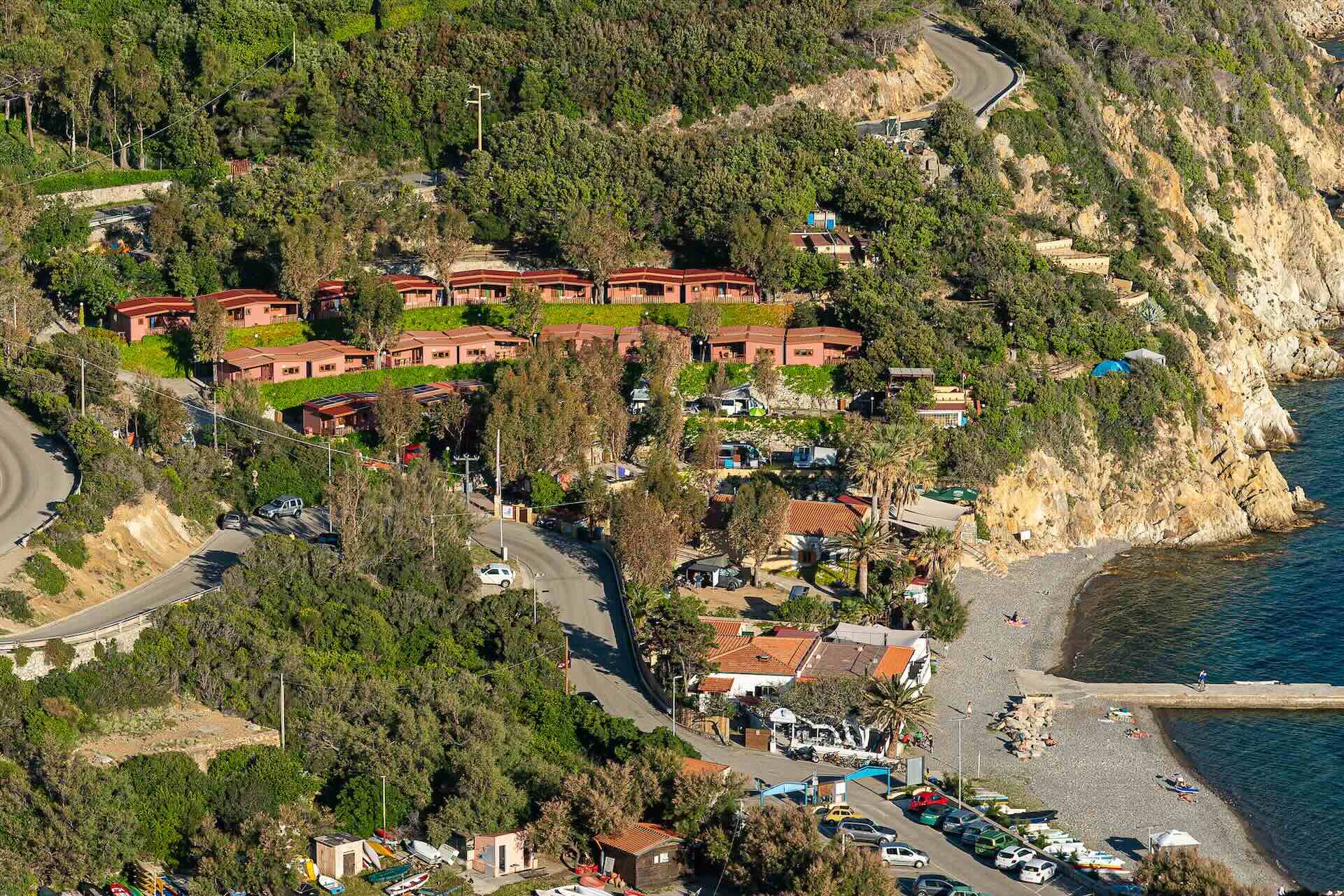 Vista aerea del Camping Enfola affacciato sul mare con spiaggia, molo e costa rocciosa dell’Isola d’Elba