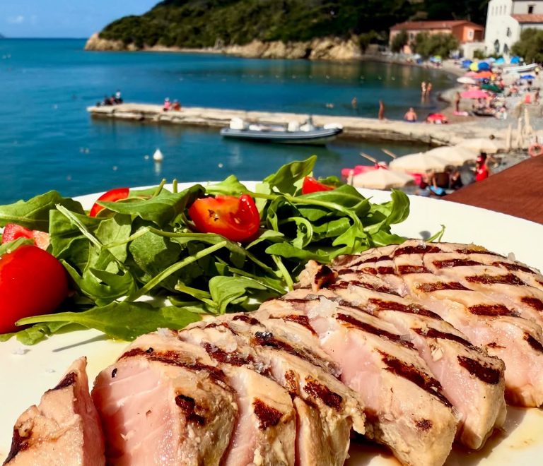 Tagliata di tonno con rucola e pomodorini servita vista mare nella baia di Enfola