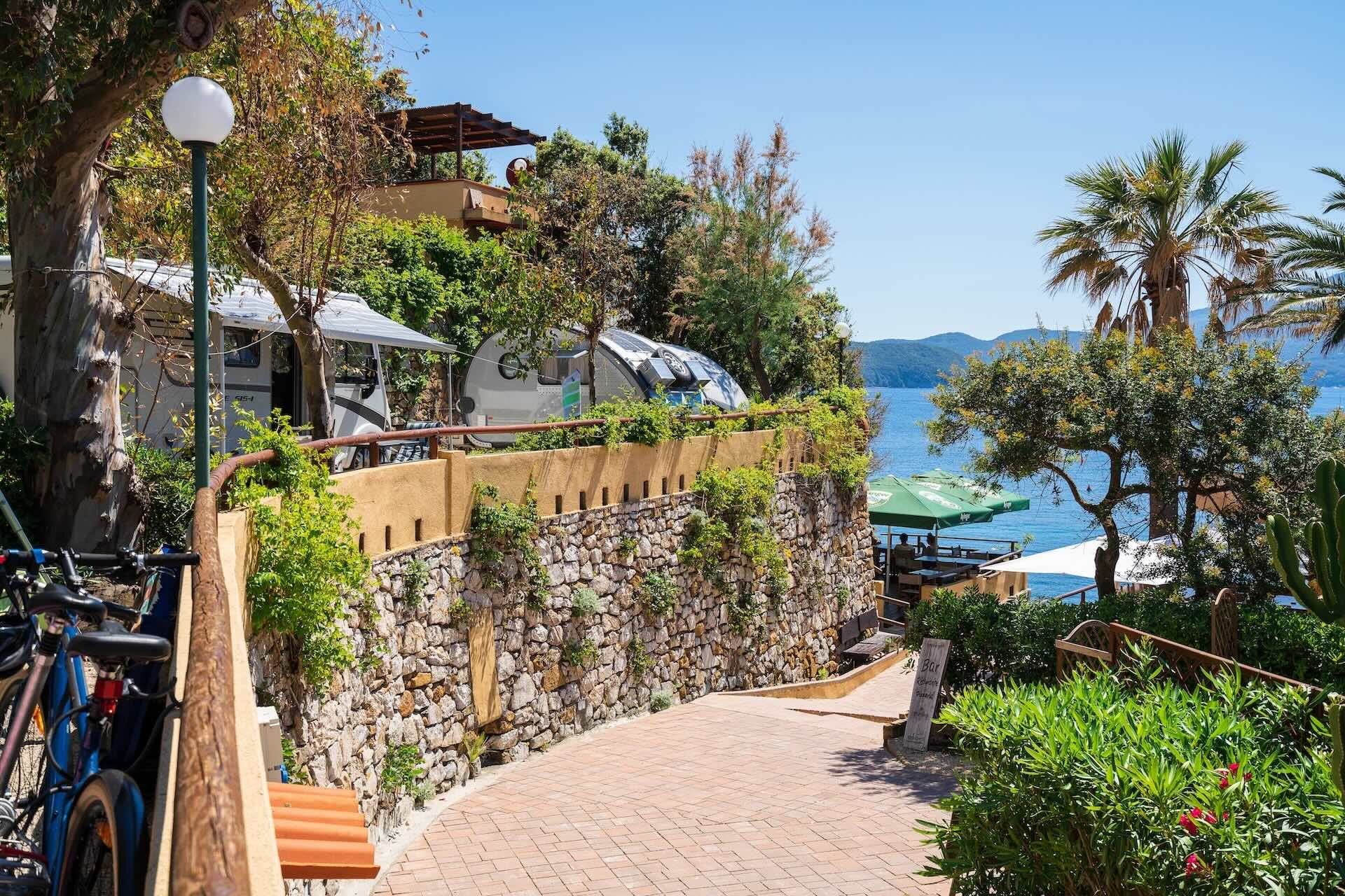 Viale pedonale interno del Camping Enfola tra vegetazione mediterranea e vista mare